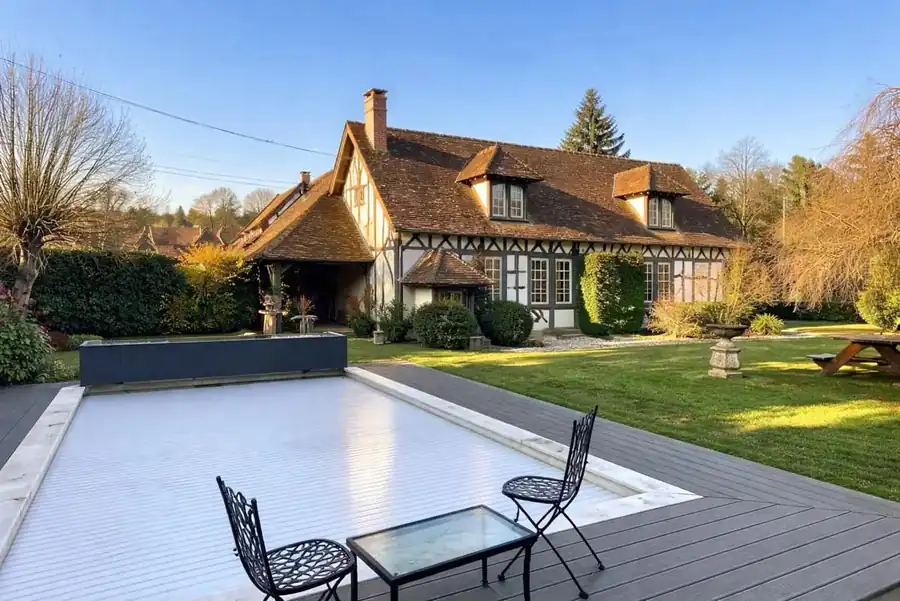 La terrasse en bois, la piscine et la maison au fond du jardin